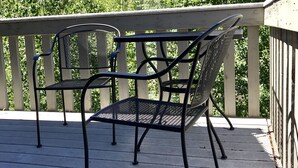 A deck with two metal chairs and a table, overlooking a forested hillside.
