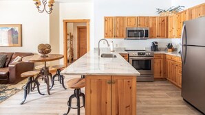 A modern kitchen with wooden cabinets, a stainless steel refrigerator, a microwave, and a built-in oven. There is a wooden island with stools and a marble countertop. - 8562 | Pool & Hot tub OPEN, Steps to Gondola. (Keystone)