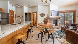 A modern kitchen with a marble countertop, wooden stools, a stone fireplace, and a TV in the living area. - 8562 | Pool & Hot tub OPEN, Steps to Gondola. (Keystone)