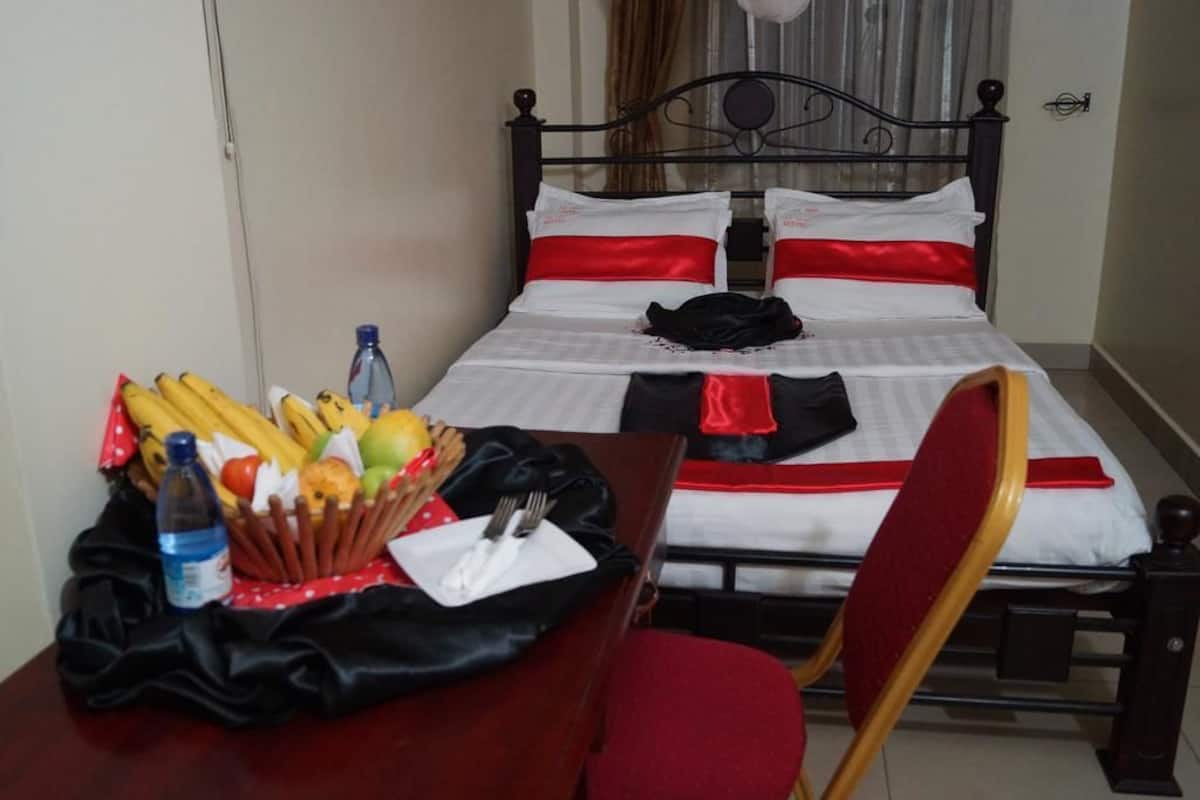 Una cama bien tendida con ropa blanca y roja, una mesita con provisiones para el desayuno y una silla.