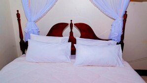 A bed with white bedding, a wooden headboard, and white curtains. - Kijungu Hill Hotel (Hoima)