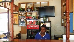 A bar area with a counter, shelves stocked with various bottles, and a television mounted on the wall. - Kijungu Hill Hotel (Hoima)