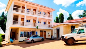 A multi-story building with balconies, a reception area, and a parked car and truck. - Kijungu Hill Hotel (Hoima)