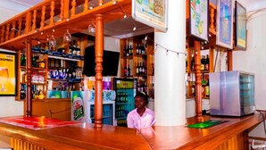 A bar area with wooden shelves stocked with various bottles, a refrigerator, and a television. - Kijungu Hill Hotel (Hoima)