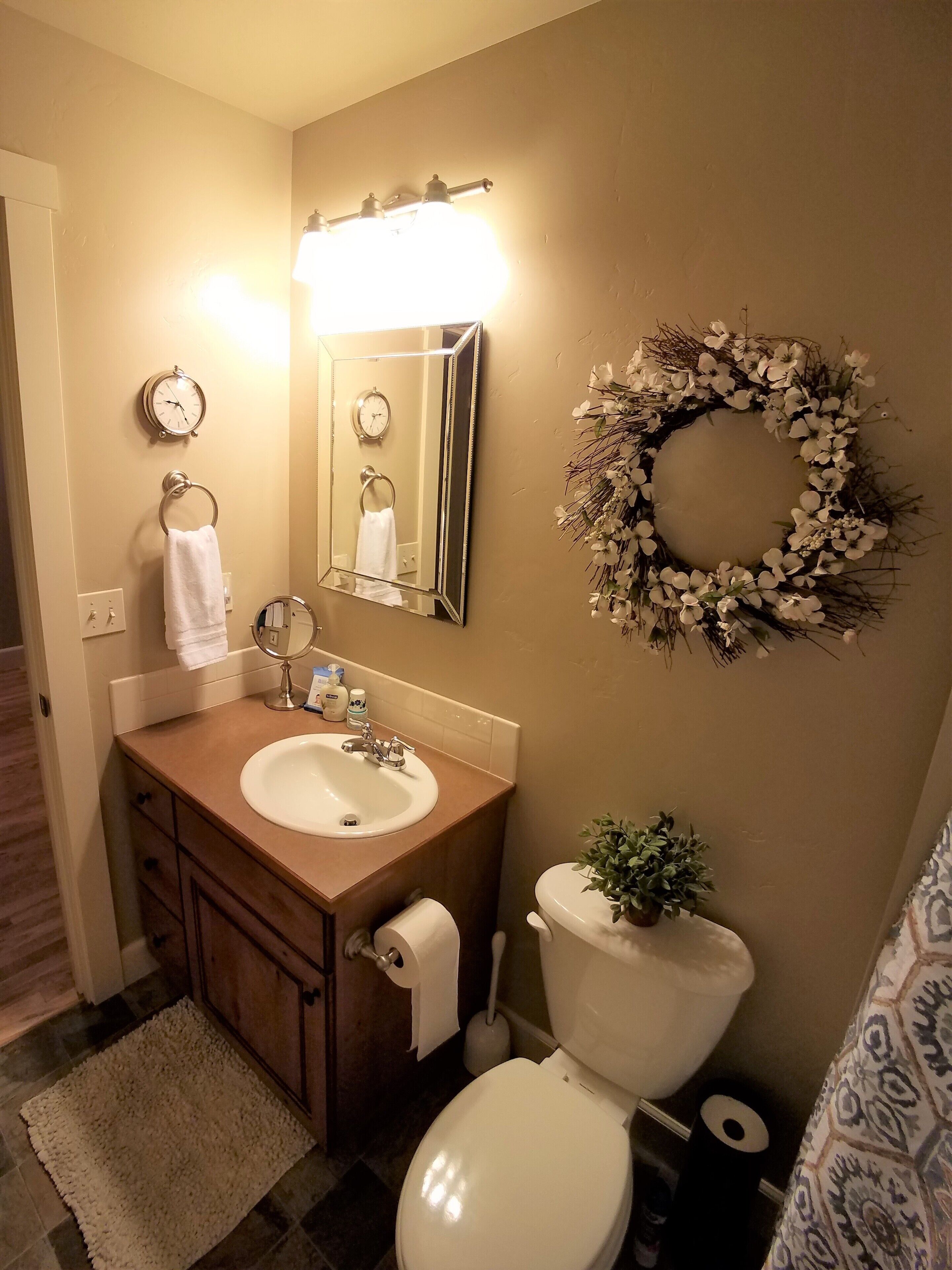 Un baño con lavamanos, espejo, inodoro y un arreglo decorativo en la pared.