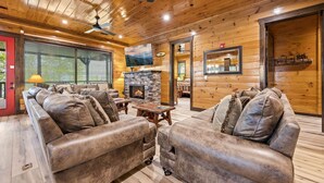 L’intérieur d’une cabane en rondins, avec une cheminée en pierre, des canapés en cuir et un ventilateur de plafond.