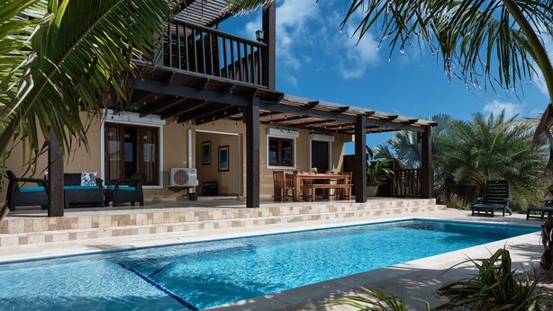 A poolside area with a covered seating area, a dining table, and a view of a building with a balcony.