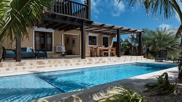 A poolside area with a covered seating area, a dining table, and a view of a building with a balcony.