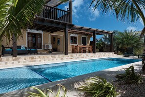 A poolside area with a covered seating area, a dining table, and a view of a building with a balcony.