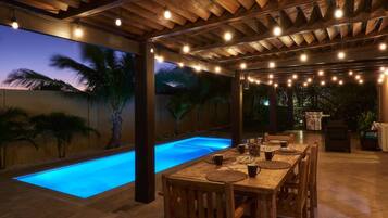 An outdoor dining area with a pool, wooden ceiling, and string lights.