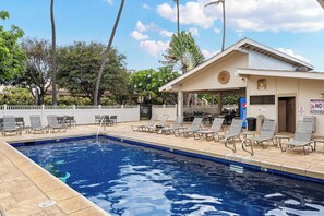 Une piscine avec des chaises longues, un espace de détente couvert et un bâtiment orné d’une horloge et d’une enseigne Pepsi.