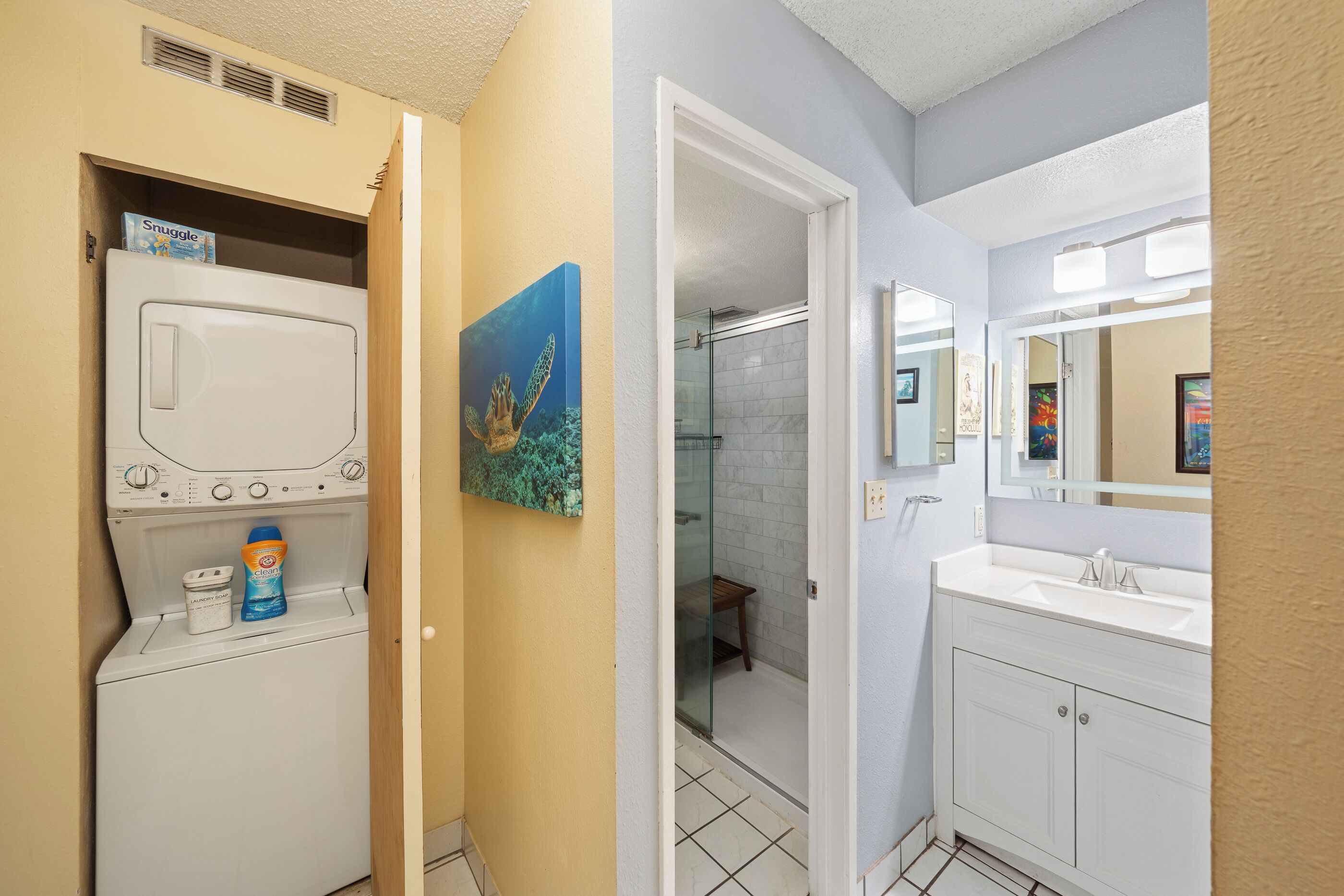 A compact bathroom with a washing machine, a shower, and a sink.
