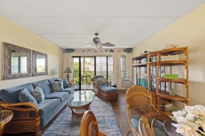 A living room with a sofa, chairs, a coffee table, a ceiling fan, and a bookshelf.