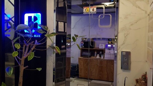 A hotel lobby with a reception desk, a blue illuminated sign, and a plant. - Blue Hotel (Geoje)