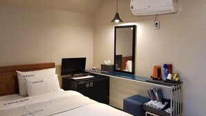 A hotel room with a bed, a bedside table with a lamp, a mirror, a radiator, and a small cabinet. - Blue Hotel (Geoje)