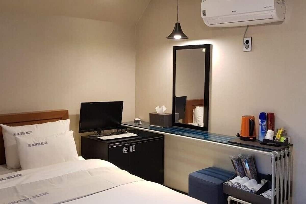 A hotel room with a bed, a bedside table with a lamp, a mirror, a radiator, and a small cabinet.
