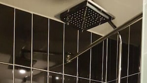 A bathroom with black tiled walls, a showerhead, and a handheld shower attachment. - Blue Hotel (Geoje)