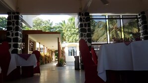 A covered outdoor area with stone pillars, tables with white tablecloths, and a view of greenery outside. - Hotel Al Amal (Mutsamudu)