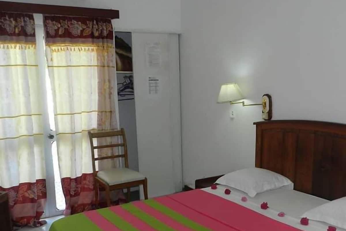 A room with a bed, a chair, an air conditioning unit, and a wall-mounted lamp.