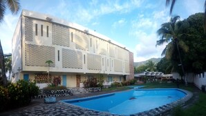 A hotel with a swimming pool, a stone pathway, and a garden area with palm trees. - Hotel Al Amal (Mutsamudu)