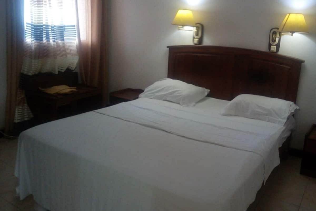 A neatly made bed with white linens, two bedside lamps, and a small wooden nightstand with a bottle on it.