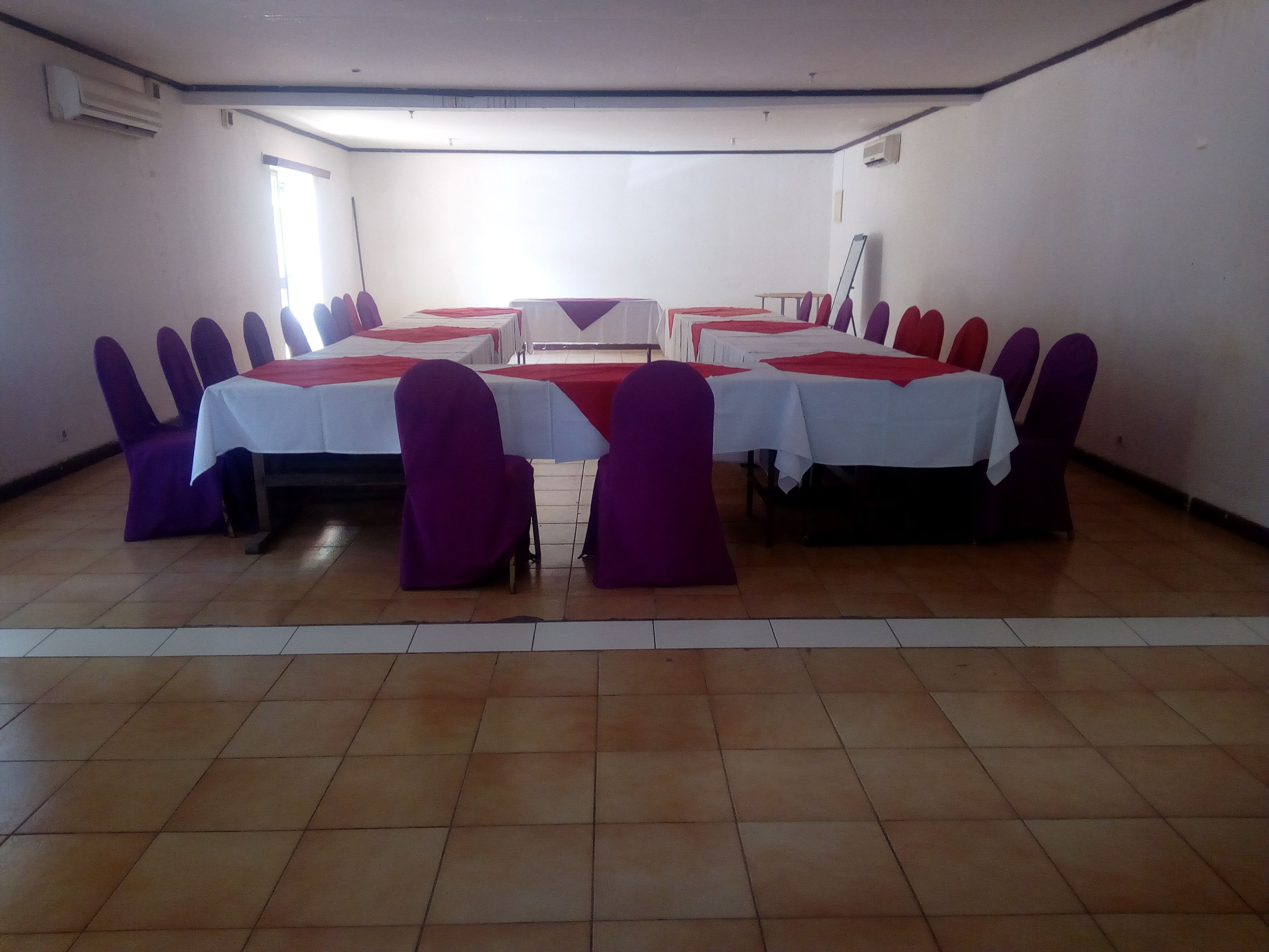 Un salón de conferencias con una mesa central rodeada de sillas, cada una cubierta con un mantel rojo y blanco.