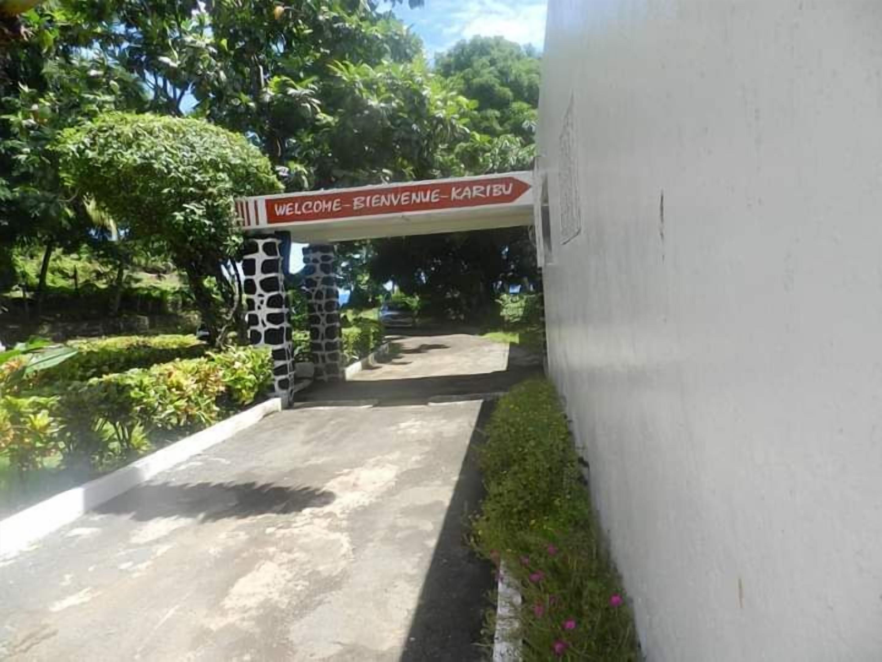 A welcome sign at the entrance of a building with a stone pillar and a paved pathway leading inside.