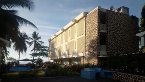 A building with a stone facade and multiple balconies, surrounded by palm trees and a pool. - Hotel Al Amal (Mutsamudu)
