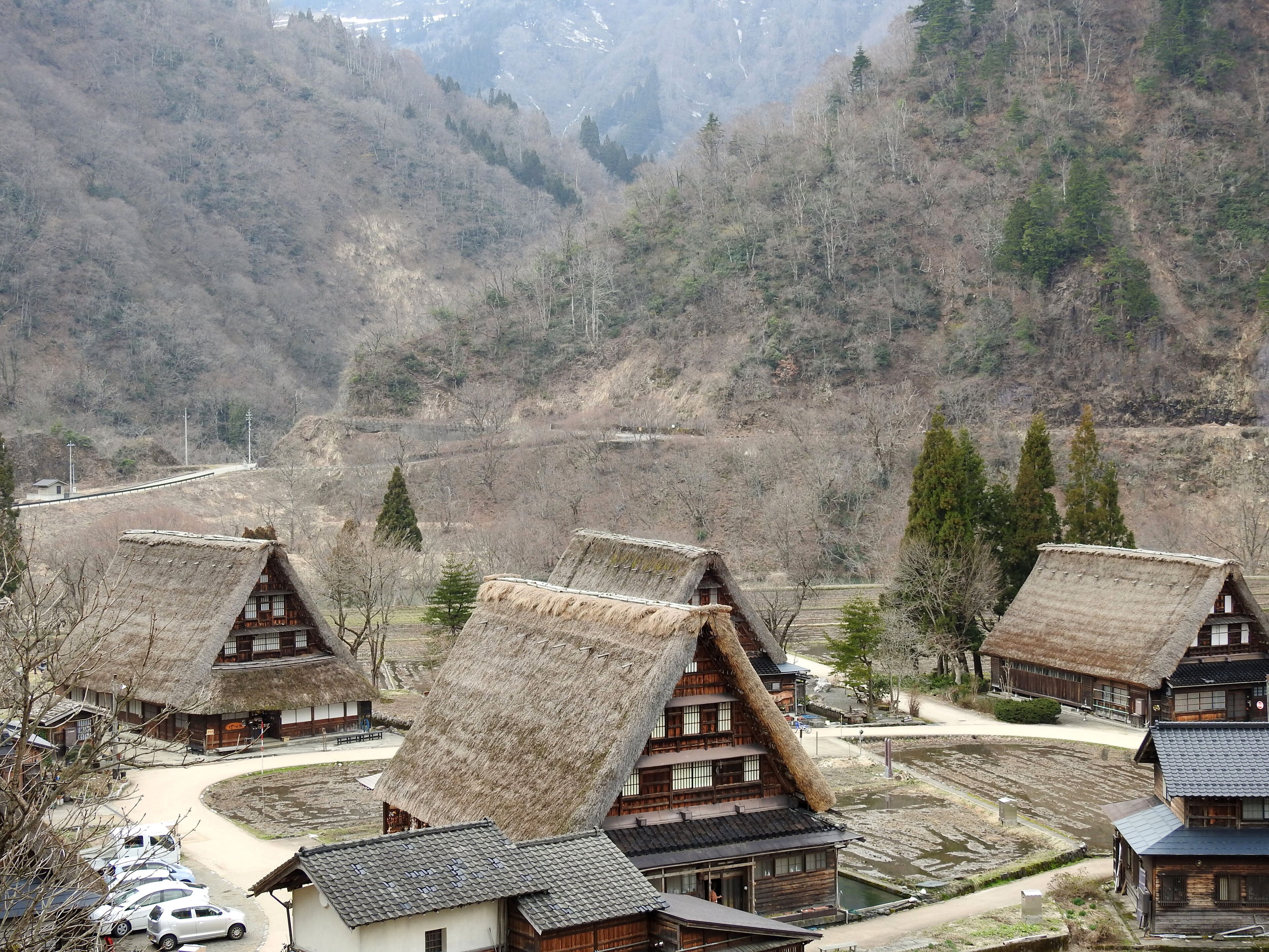 Traditional wooden houses with thatched roofs, arranged in a village setting with a mountainous backdrop.