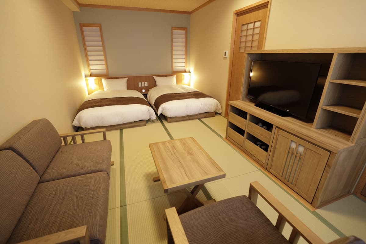 Ein Hotelzimmer mit zwei Betten, einem Fernseher, einem Sofa und einem kleinen Tisch.