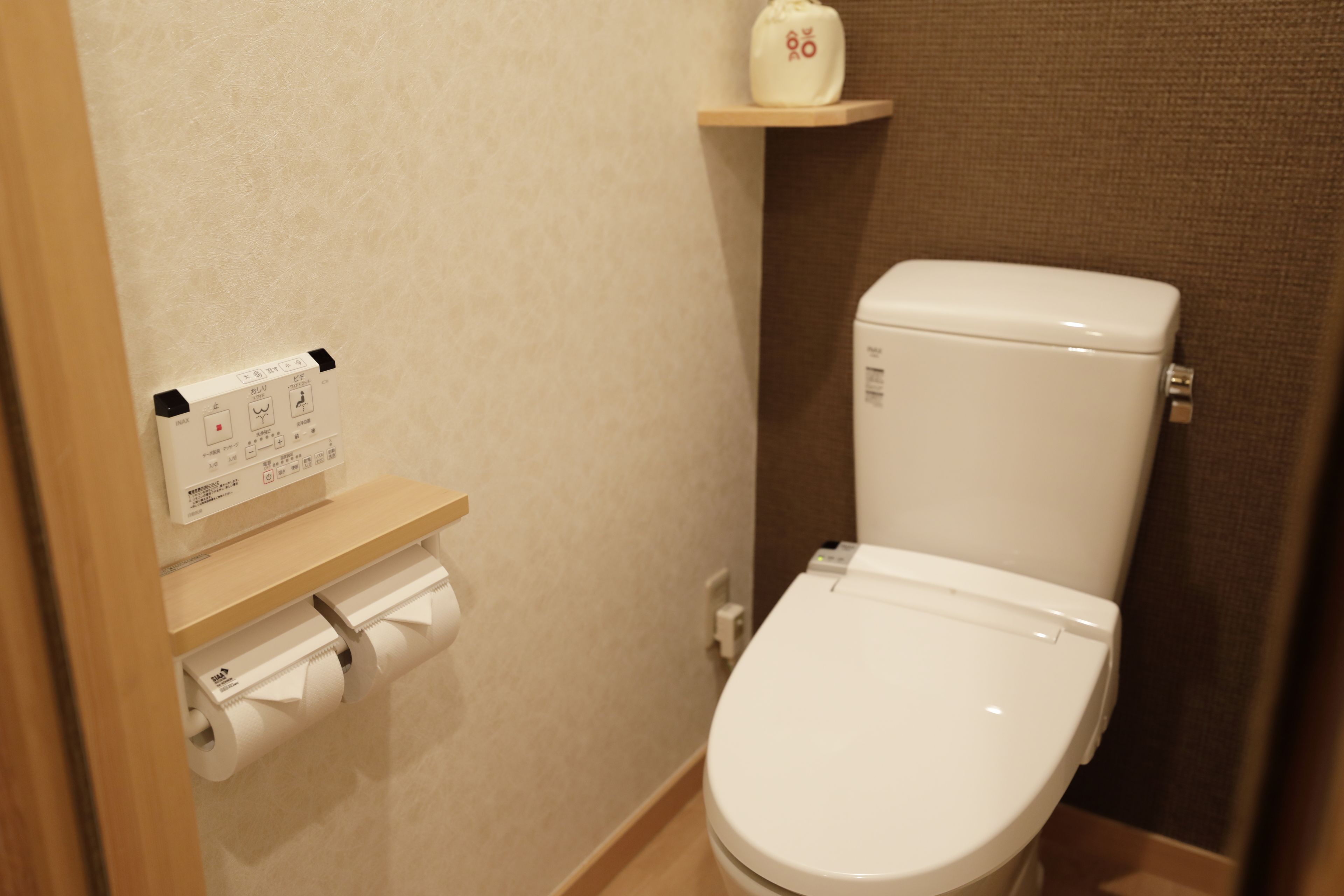 A small bathroom with a toilet, a toilet paper holder, and a shelf with a bottle.