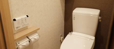 A small bathroom with a toilet, a toilet paper holder, and a shelf with a bottle.