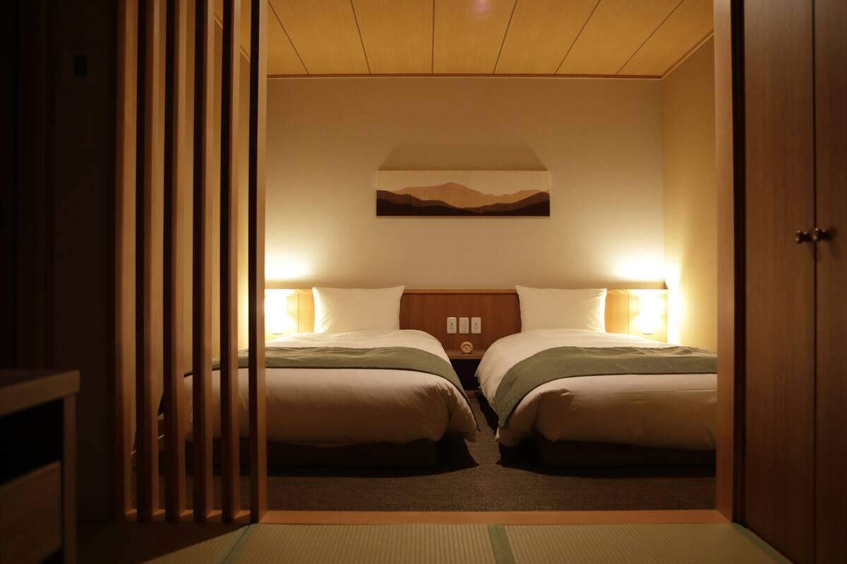 Ein Hotelzimmer mit zwei Betten, einem Holzkopfteil, einem Nachttisch und einem an der Wand hängenden Gemälde.