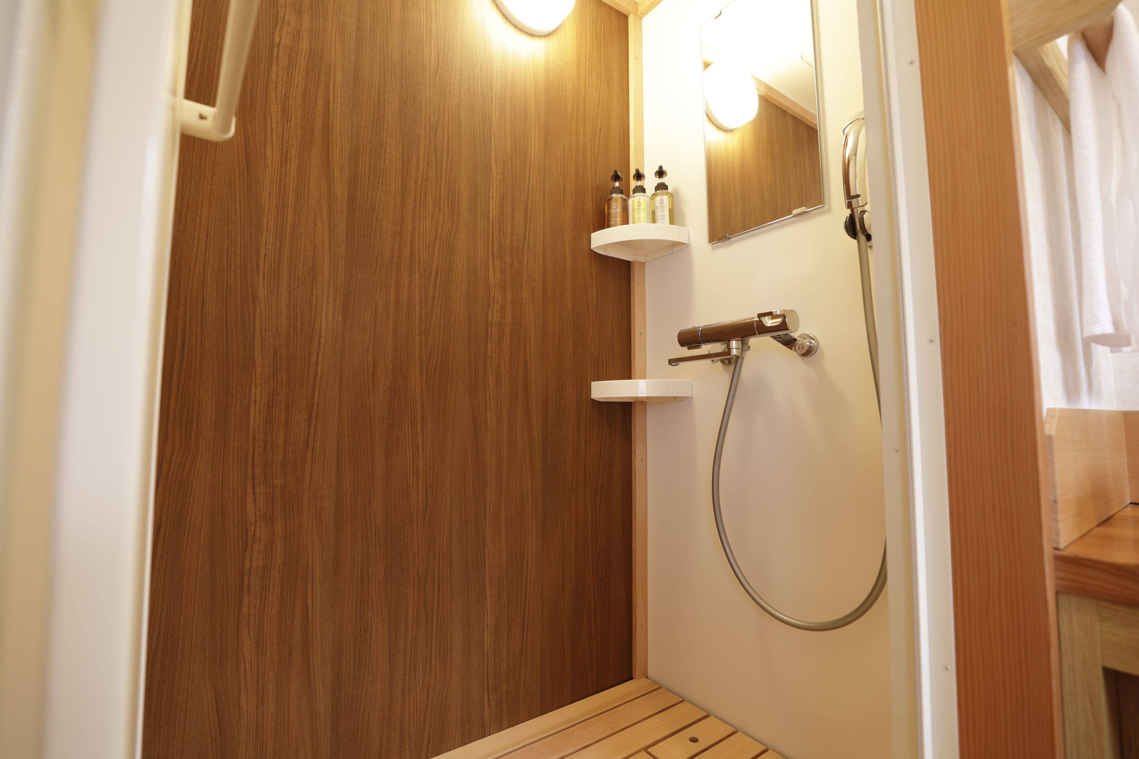 Een houten badkamer met een douche, een spiegel en een plank met toiletartikelen.