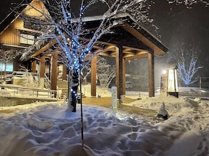 A snow-covered outdoor area with a wooden building, a tree with blue lights, and a snow-covered ground. - Onyado Yuinosho (Shirakawa)