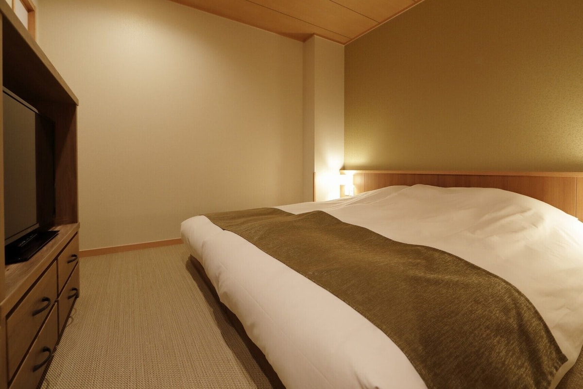 A hotel room with a bed, a television, and a bedside table.