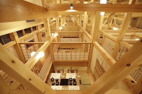 A multi-level wooden structure with a central open area featuring tables and chairs, surrounded by wooden railings and multiple levels of balconies.