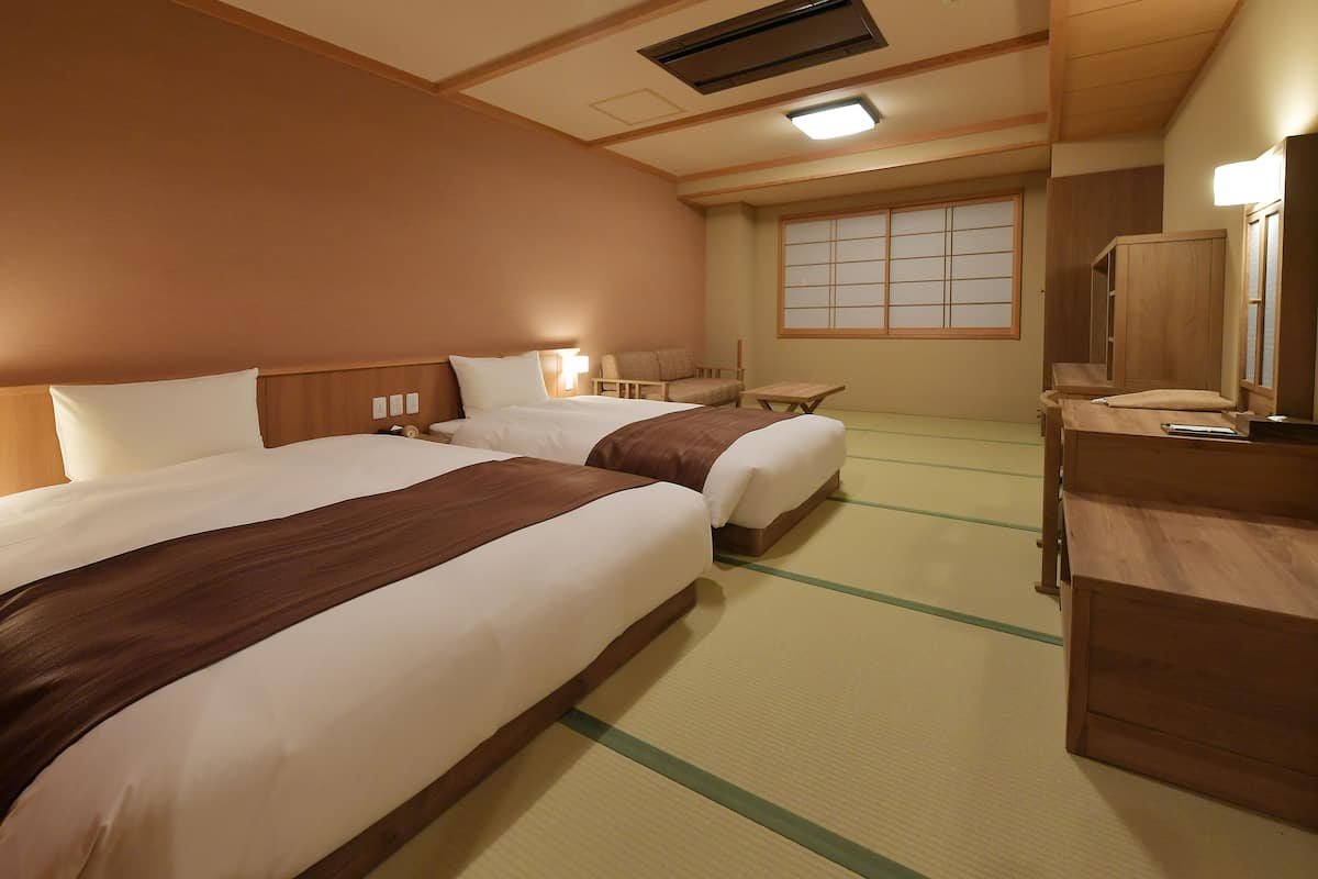 Ein Hotelzimmer mit zwei Betten, einem Schreibtisch, einem Stuhl, einem Kleiderschrank und einer traditionellen Schiebetür.
