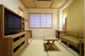 A traditional Japanese-style room with tatami flooring, a television on a wooden stand, a low table, a sofa, and a sliding door with a window.