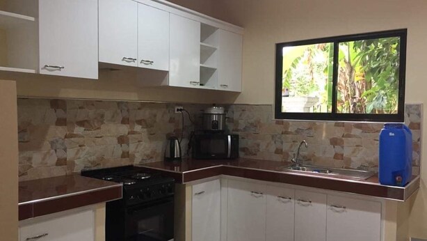 A kitchen with white cabinets, a stove, a microwave, and a sink. - Cris Place Dumaguete (Valencia)