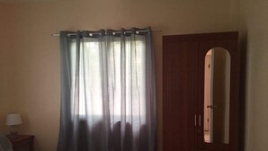A bedroom with a bed, a wooden wardrobe, and a window with sheer curtains. - Cris Place Dumaguete (Valencia)