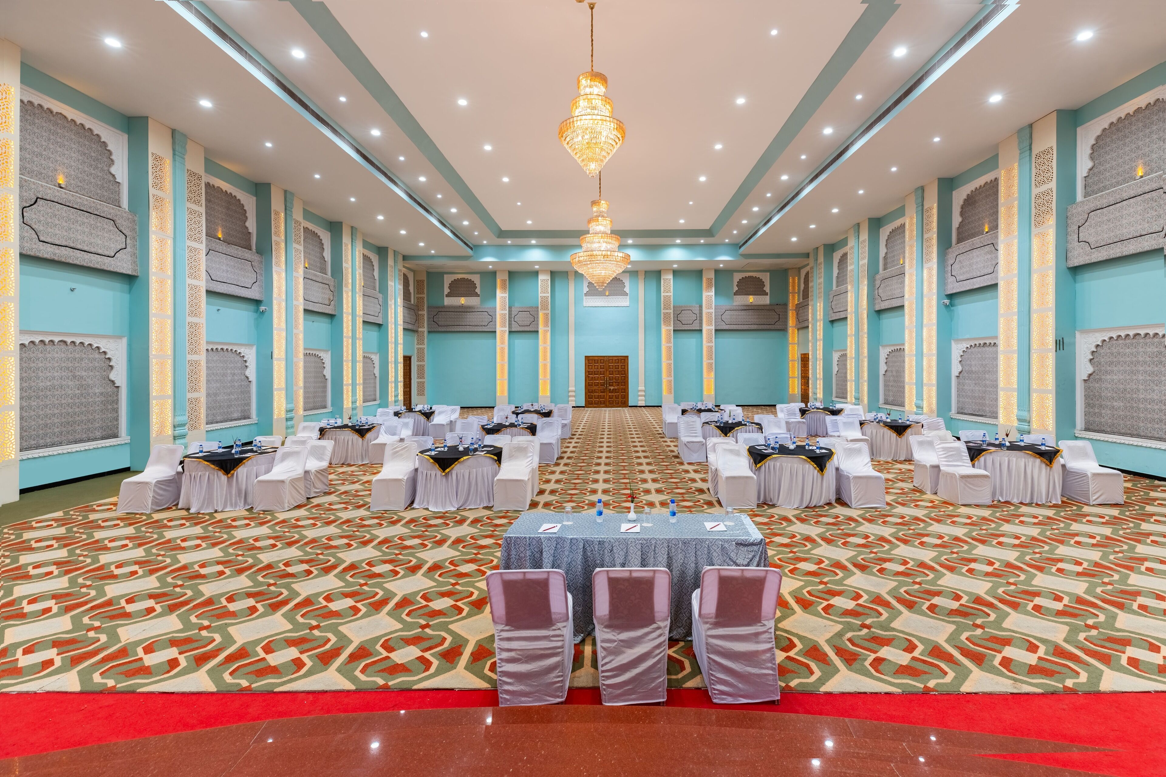 A large conference room with a patterned carpet, rows of tables with chairs, and a chandelier.