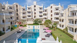 Un hotel con varias edificaciones blancas, una piscina central y zonas de estar al aire libre.