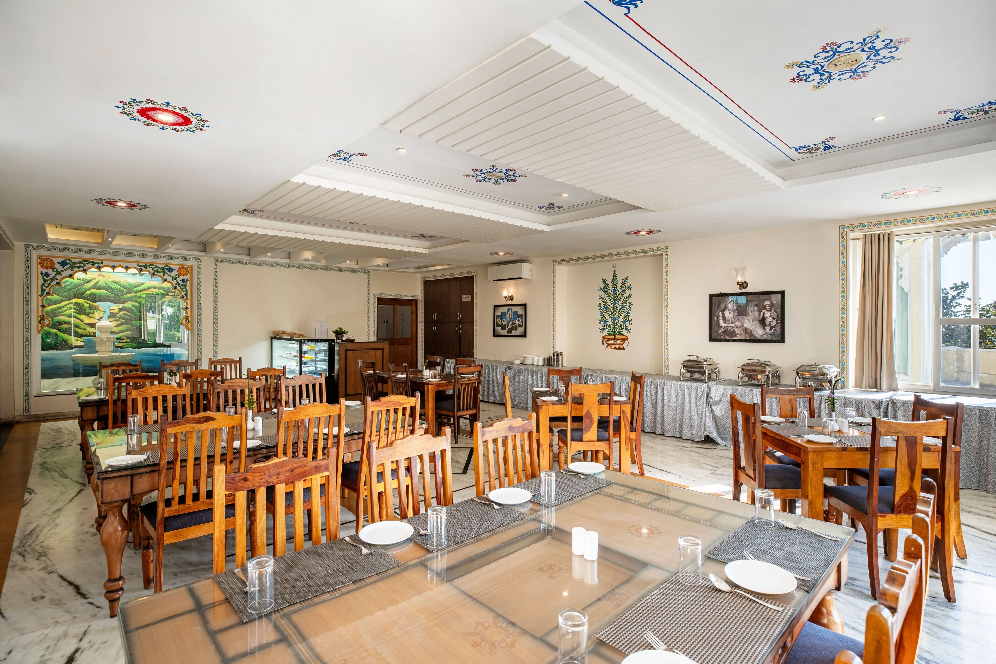 Un comedor con mesas y sillas de madera, un mural grande en la pared y un techo con diseños decorativos.