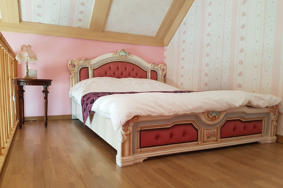 A bedroom with a classic four-poster bed, a small bedside table, and a chandelier.