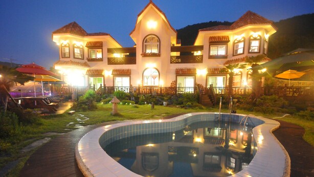A large, two-story house with a swimming pool, surrounded by a wooden deck and a well-maintained lawn. - Red Praha Pension (Geoje)
