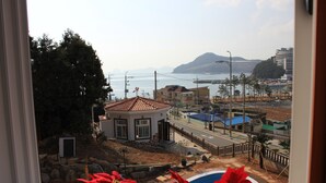A view from a window overlooking a residential area with a swimming pool, a small building, and a distant mountain. - Red Praha Pension (Geoje)