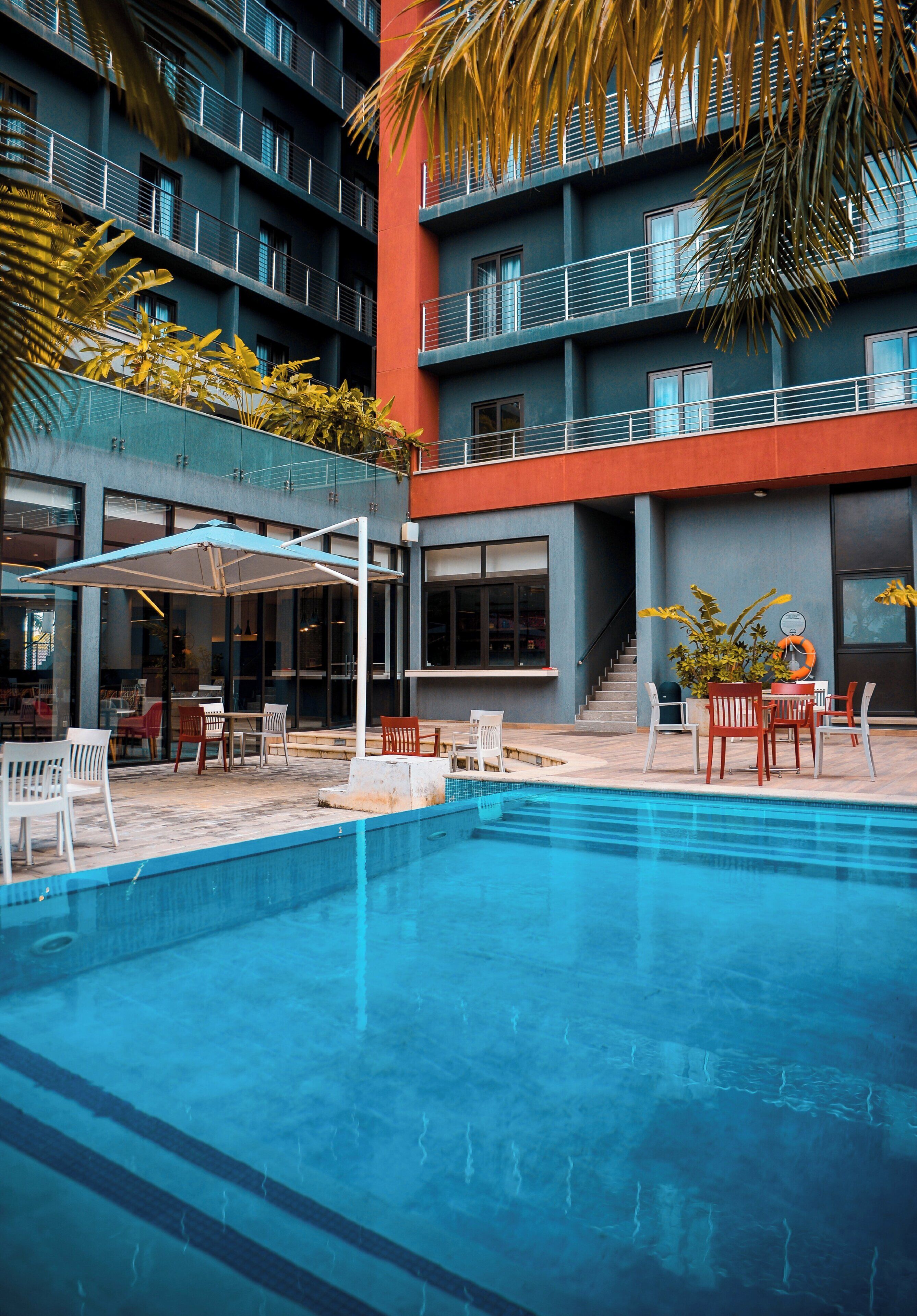 A modern hotel with a swimming pool, outdoor seating, and a staircase leading to the upper floors.