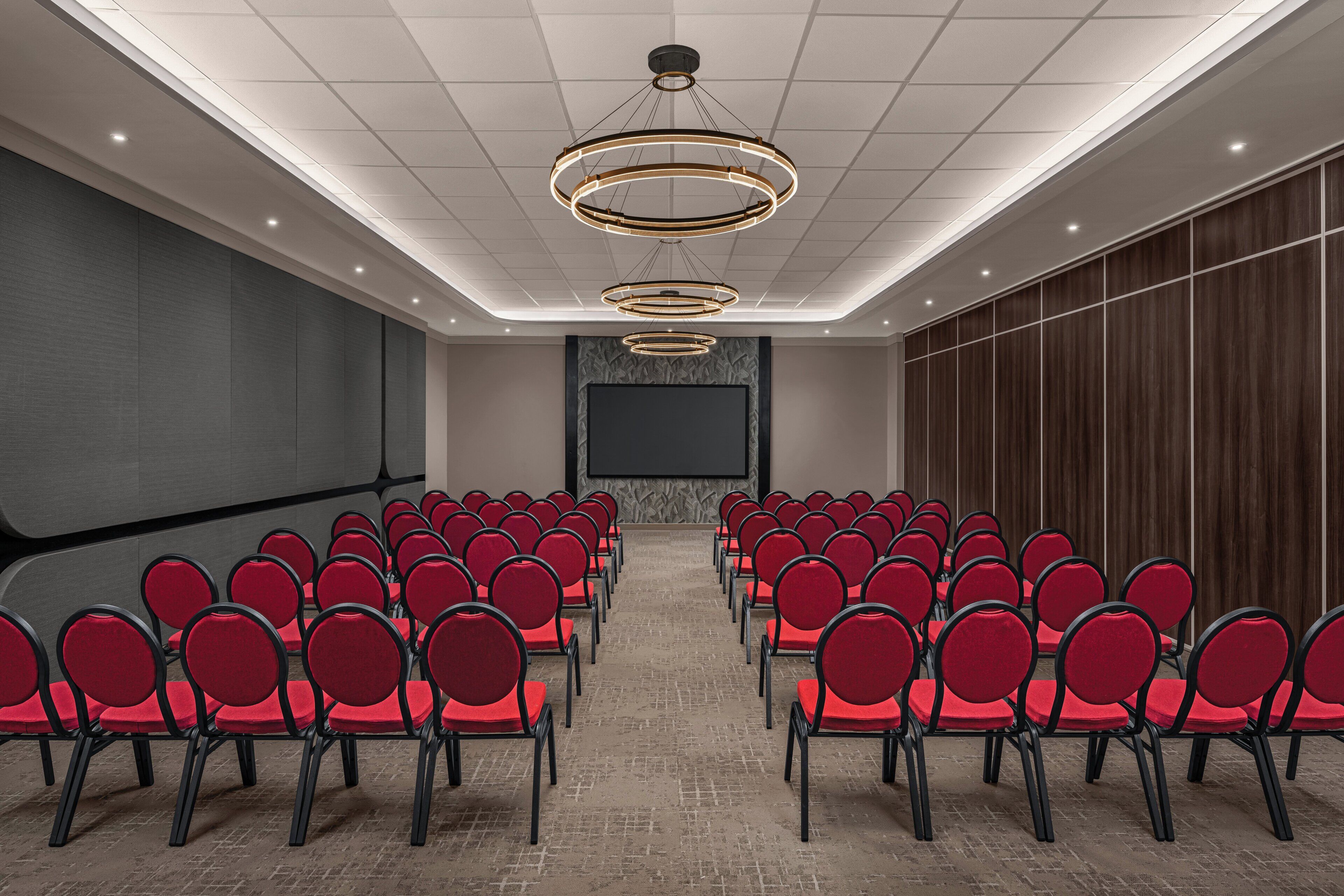 A conference room with rows of red chairs, a large screen, and a patterned wall.