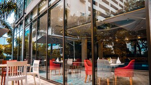 An outdoor seating area with tables and chairs, a pool, and a glass wall reflecting the surroundings. - Crowne Plaza Dar es Salaam by IHG (Dar es Salaam)